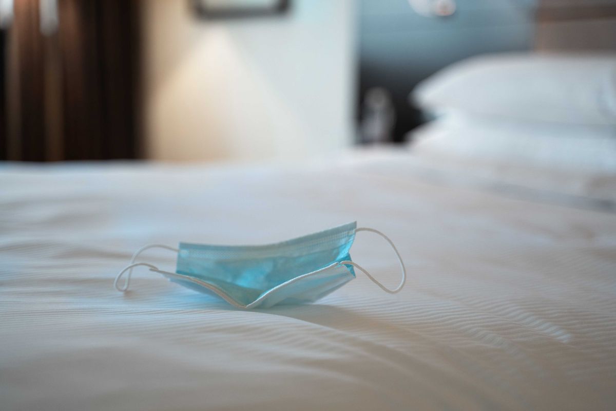 Medical mask lying on a bed in hotel suite