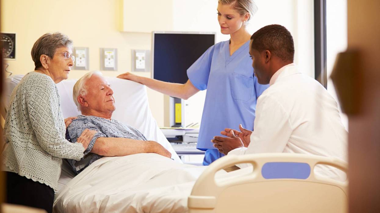 Medical Team Meeting With Senior Couple In Brightly Lit Hospital Room