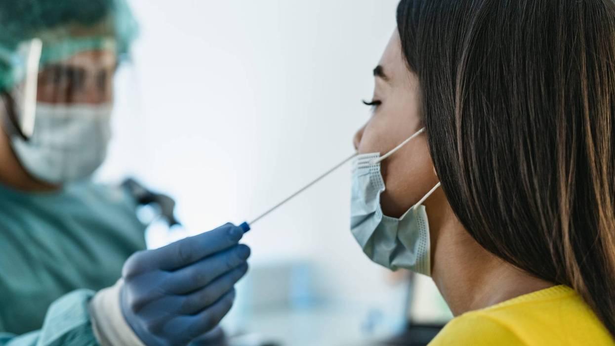 Medical worker wearing personal protective equipment doing corona virus swab on female patient - Covid19 test and health care concept