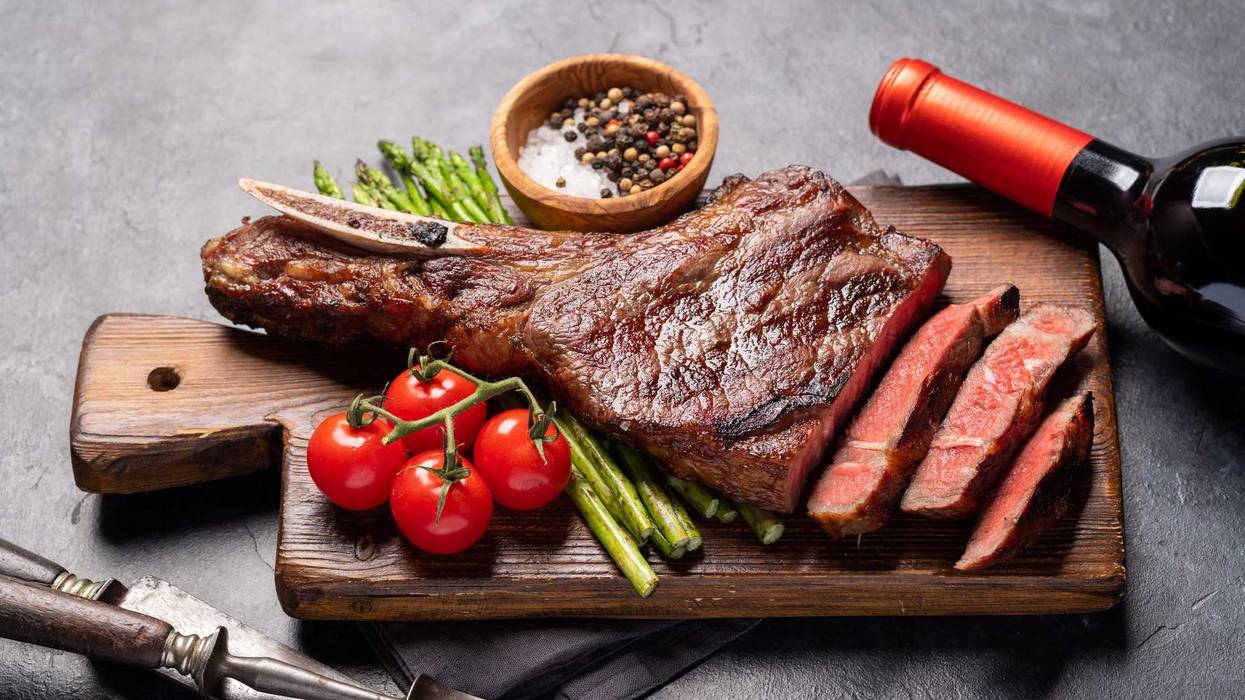 Medium rare grilled Tomahawk beef steak with asparagus and red wine