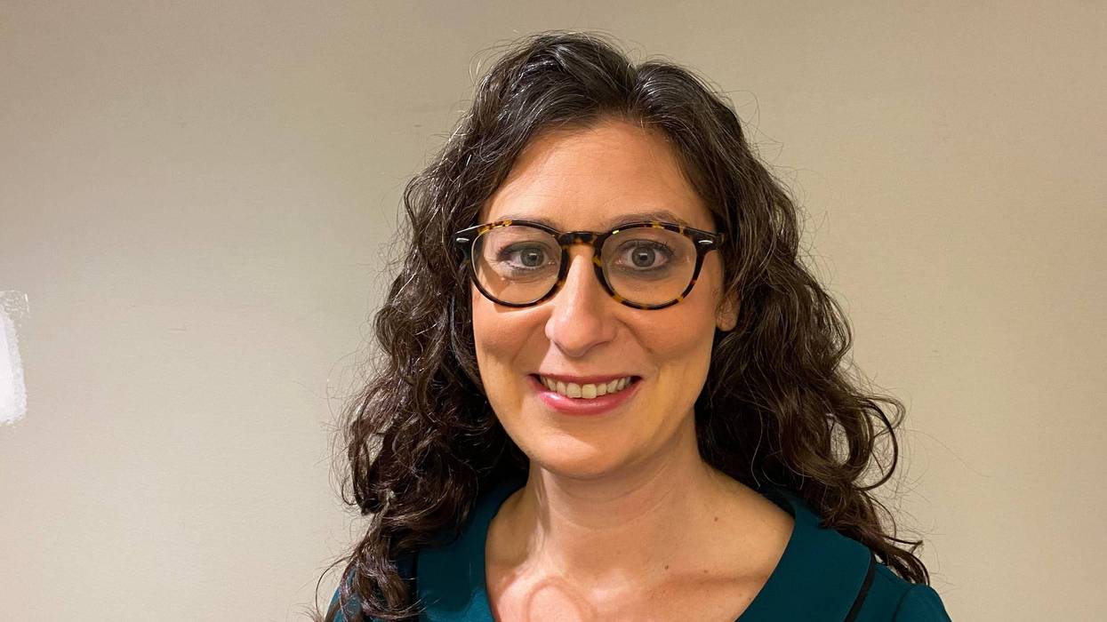 megan green smiles she has curly dark hair and glasses