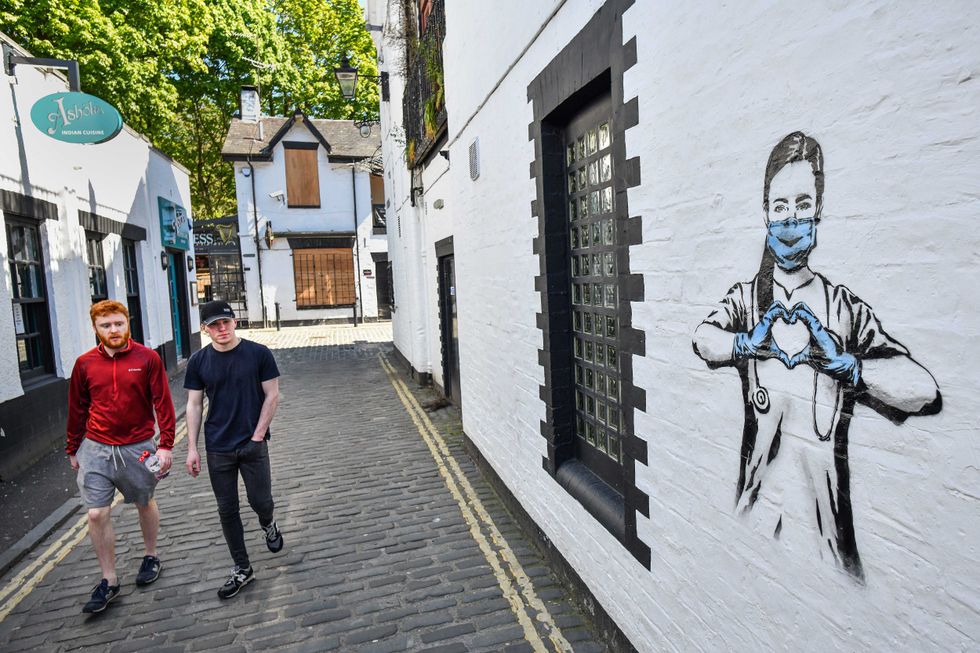 Members of the public walk past graffiti in the West End during the coronavirus lockdown on May 6, 2020 in Glasgow, Scotland. on May 06, 2020 in Glasgow. The country continued quarantine measures intended to curb the spread of Covid-19, but the infection rate is falling, and government officials are discussing the terms under which it would ease the lockdown.