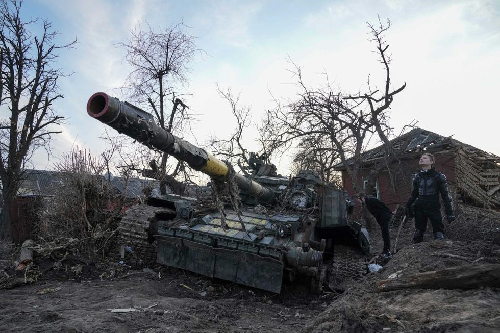 Men stand next to a destroyed tank in Chernihiv, Ukraine, Thursday, April 7, 2022