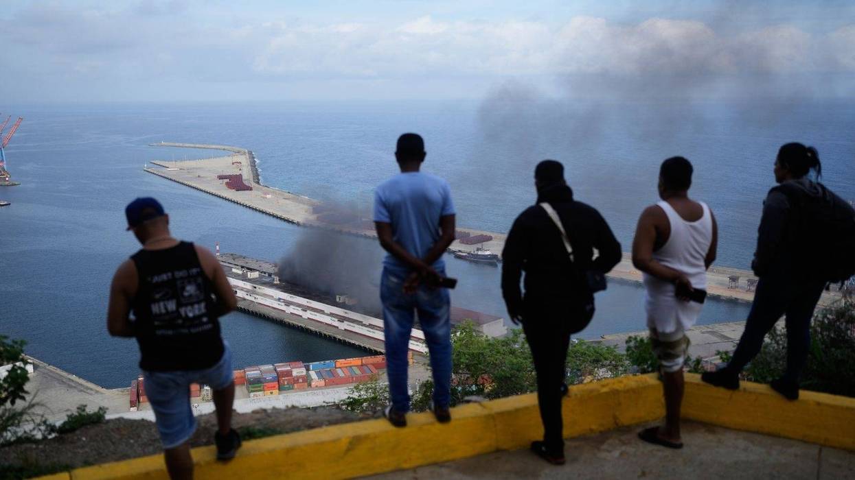 Men watch smoke rising from a dock after explosions were heard at La Guaira port, Venezuela