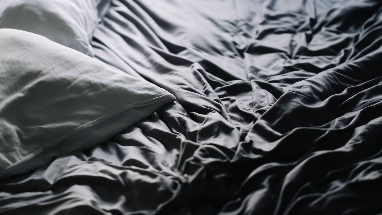 Messy wrinkled bed sheets with pillow. Dark bedroom interior detail. Crumpled fabric texture in soft light. Morning atmosphere of rest.
