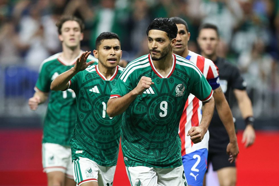 Mexican soccer players in green Aztec calendar jerseys reacting on the field.