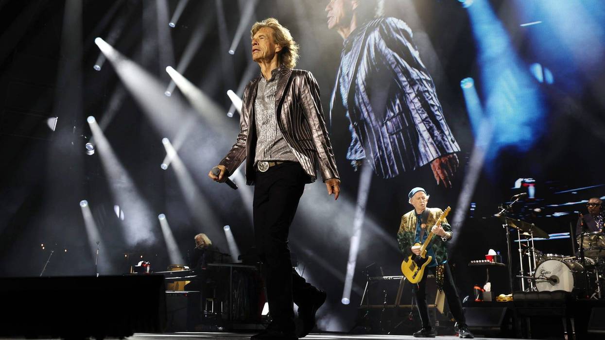 Mick Jagger walks on stage in a metallic jacket, Keith Richards plays guitar during a concert.