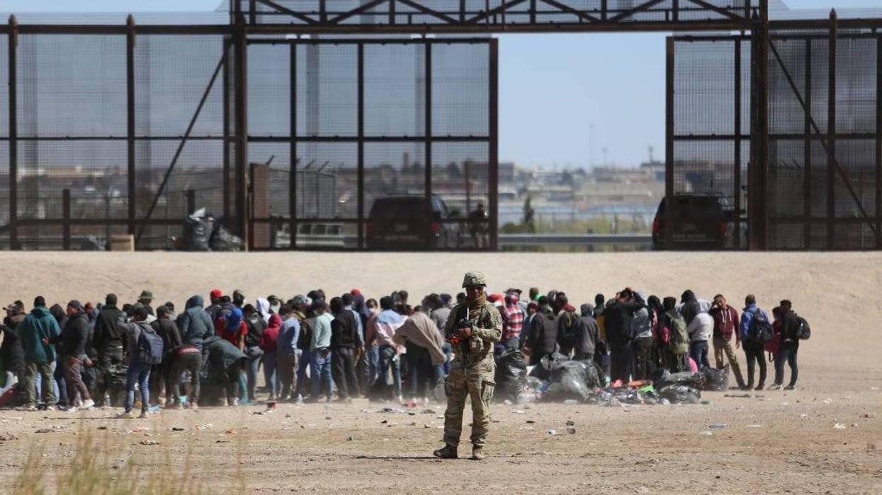 Migrants who crossed the border trough the Rio Bravo from Mexico into the U.S. wait next to the U.S. border wall where U.S. Border Patrol agents stand guard on March 30, 2023 in Ciudad Juarez, Mexico.