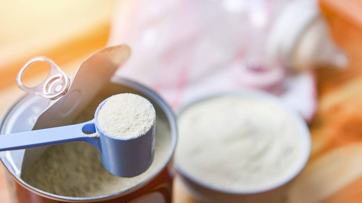 Milk powder in spoon with can and baby bottle milk in bowl on wooden table background