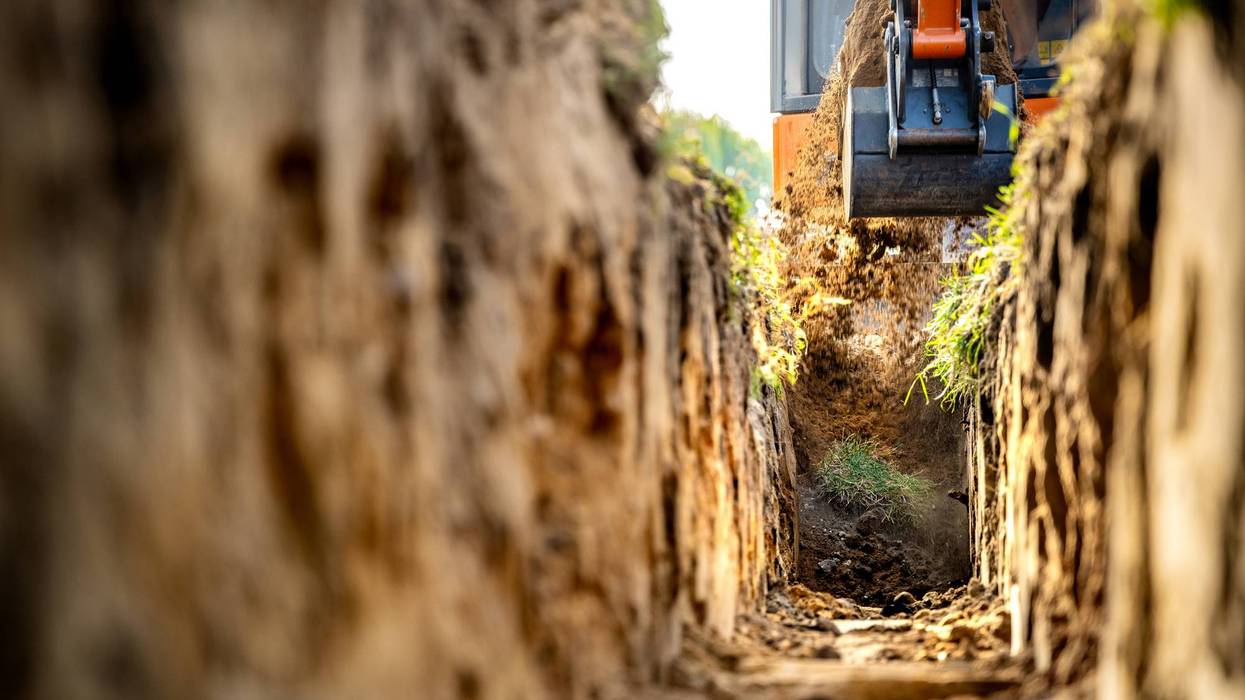 Mini excavator lifting soil from trench at construction site