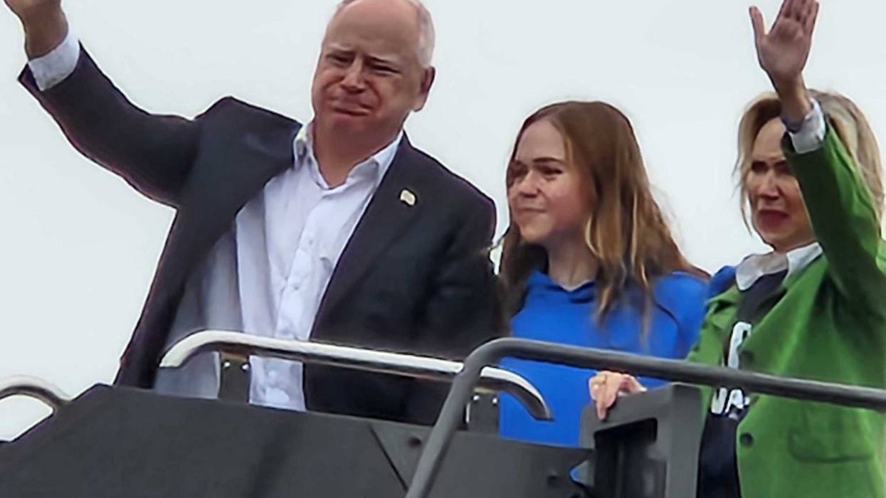 Minnesota Governor and Vice Presidential Candidate Tim Walz waves at onlookers as he boards a plane at MSP Airport with daughter Hope and wife Gwen.