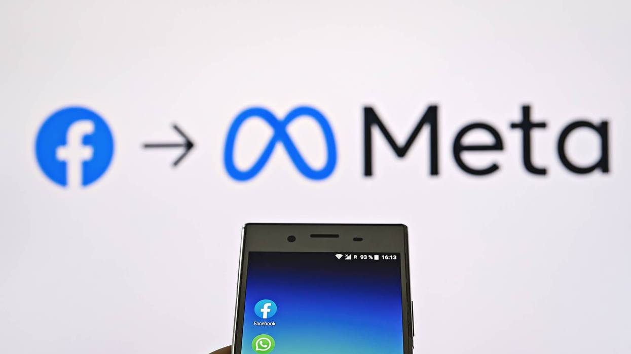 Mobile display with logo of Facebook, WhatsApp and Instagram apps in hand against blurred META logotype on white monitor