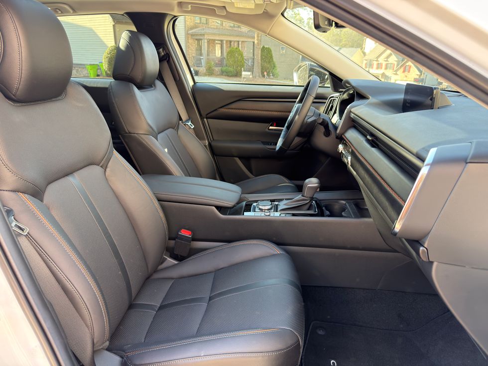 Modern car interior with black leather seats, orange stitching, dashboard, and console.
