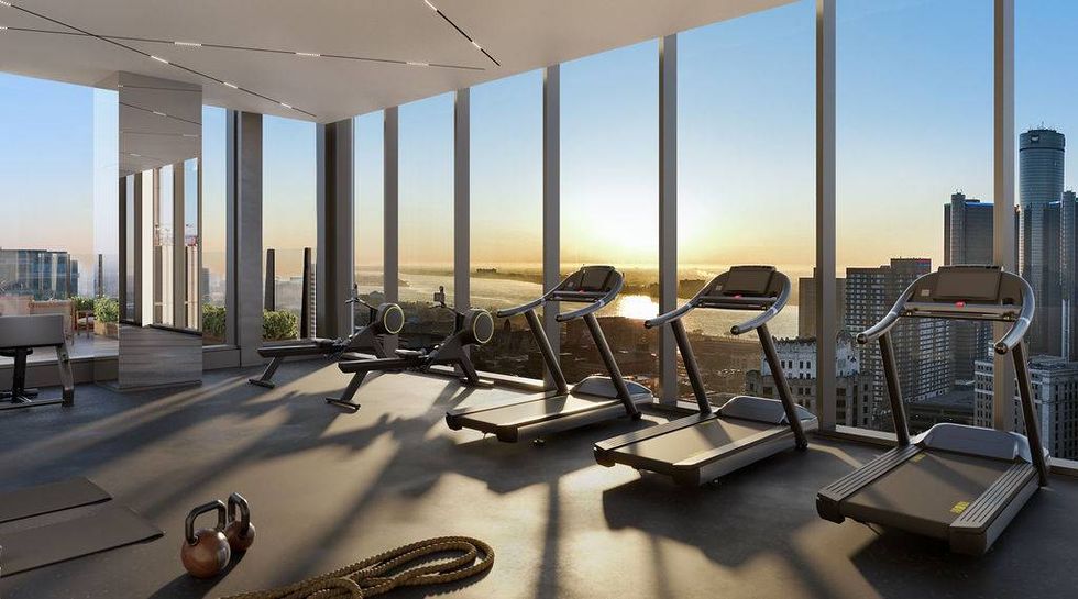 Modern gym with treadmills and rowing machine, overlooking a city skyline and river at sunset.