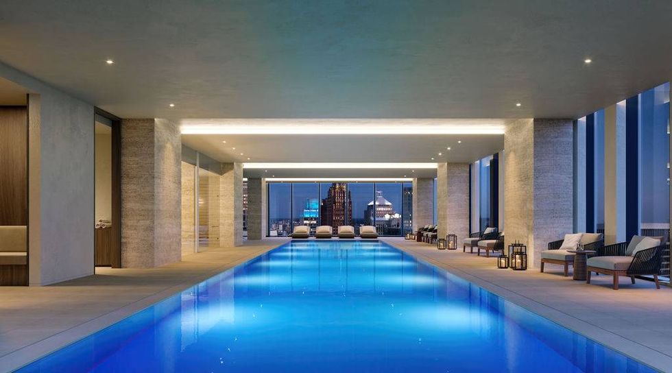 Modern indoor pool with city skyline view, glowing blue water, and lounge area.