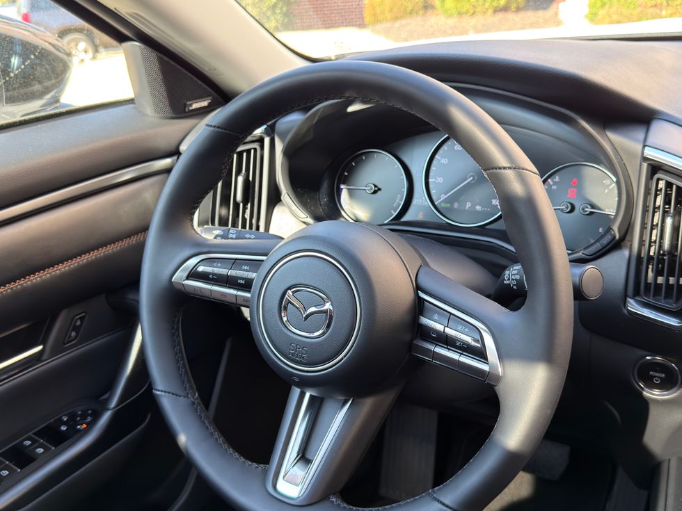 Modern Mazda car interior with black leather steering wheel, dashboard, and door panel with Bose speaker.