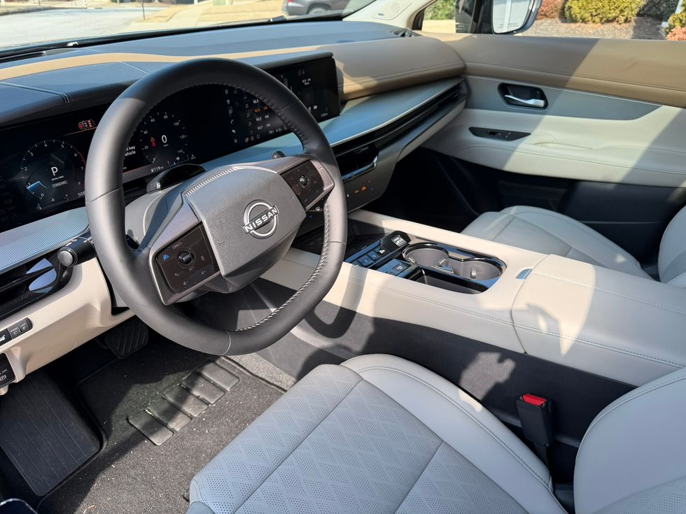 Modern Nissan car interior: black steering wheel, dual digital displays, light beige seats.