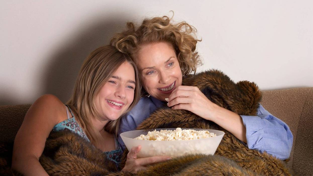 Mother and daughter (13-15) on sofa sharing popcorn, laughing
