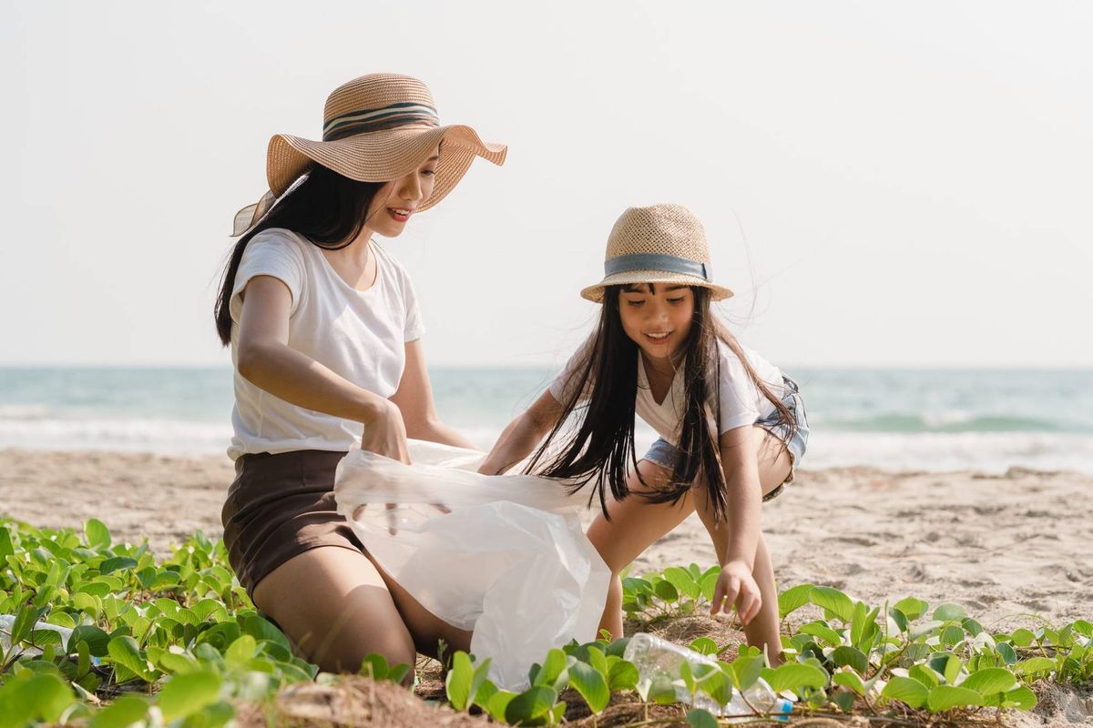 Mother and daughter picking up trash by beach