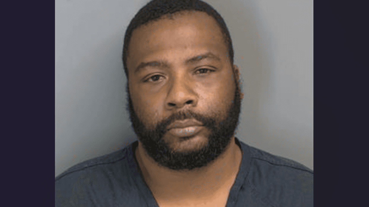 Mugshot of a Black man with a dark beard, short hair, and a dark shirt.