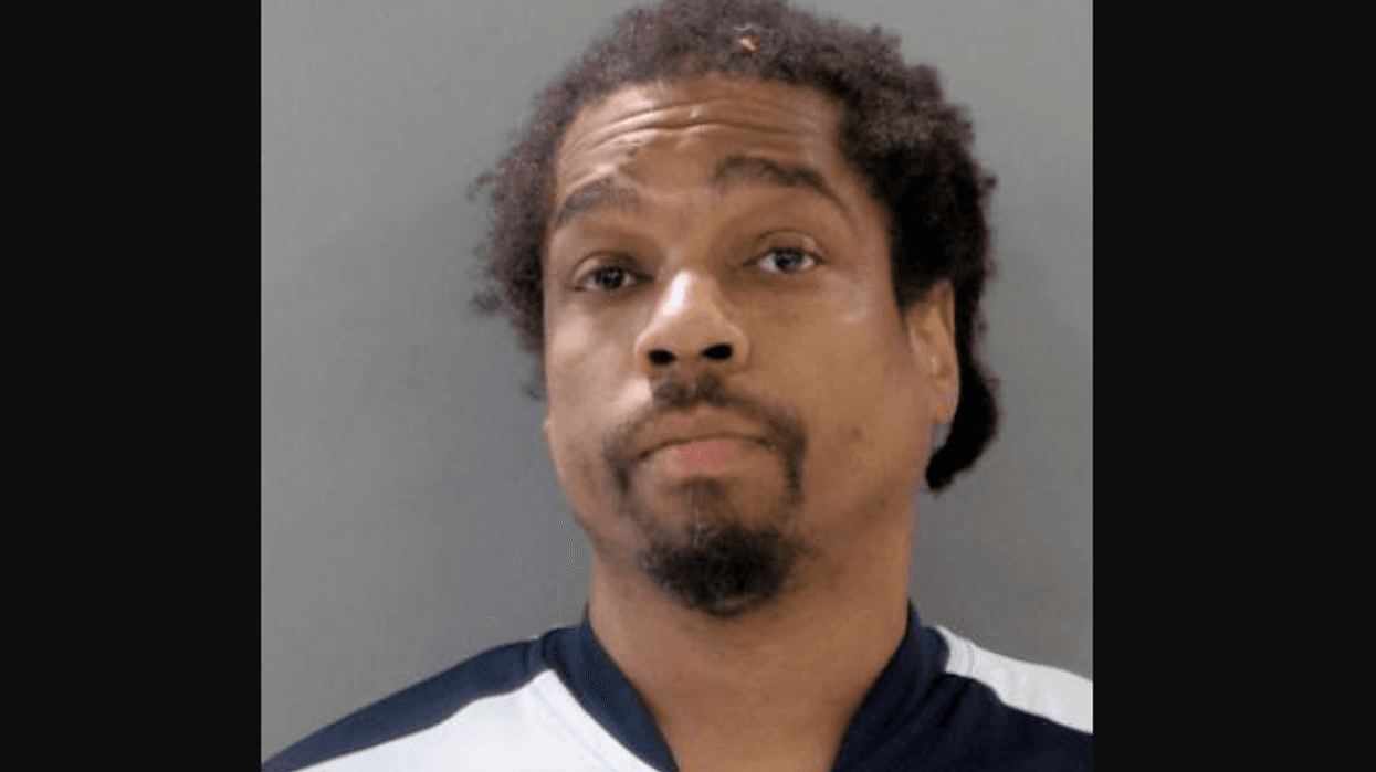 Mugshot of a Black man with curly hair and a goatee, wearing a two-tone shirt.