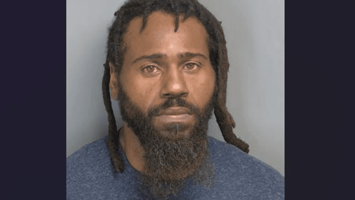 Mugshot of a man with dark dreadlocks and a full beard, wearing a blue shirt.