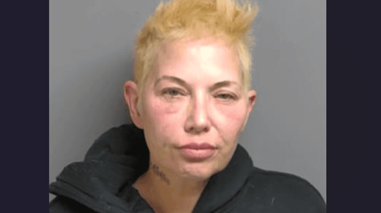 Mugshot of a person with blonde spiky hair, pale skin, redness around eyes, and neck tattoo.