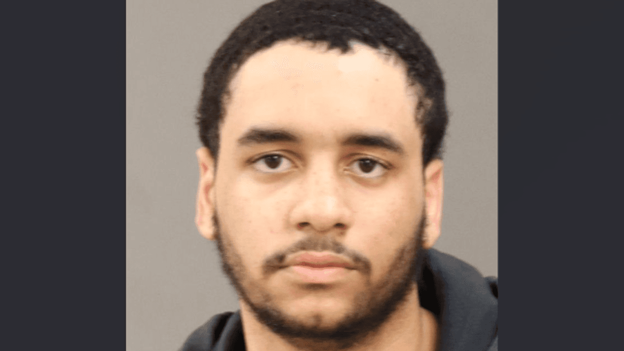 Mugshot of a young man with dark wavy hair, light beard, and dark hooded sweatshirt.