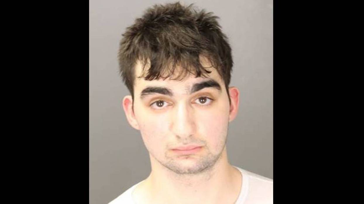 Mugshot of a young man with messy dark hair, thick eyebrows, and a neutral expression.