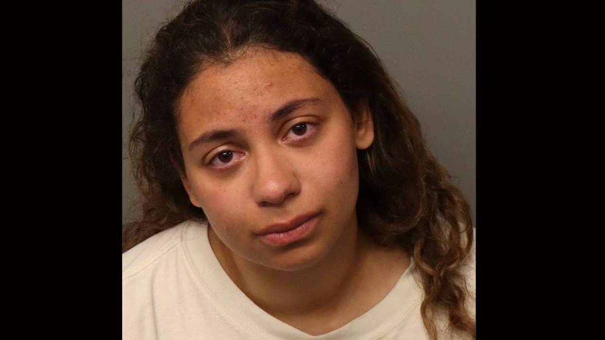 Mugshot of a young woman with long wavy brown hair, red eyes, and facial blemishes.