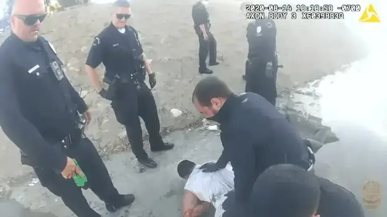 multiple police officers stand around while one kneels on the back of a man