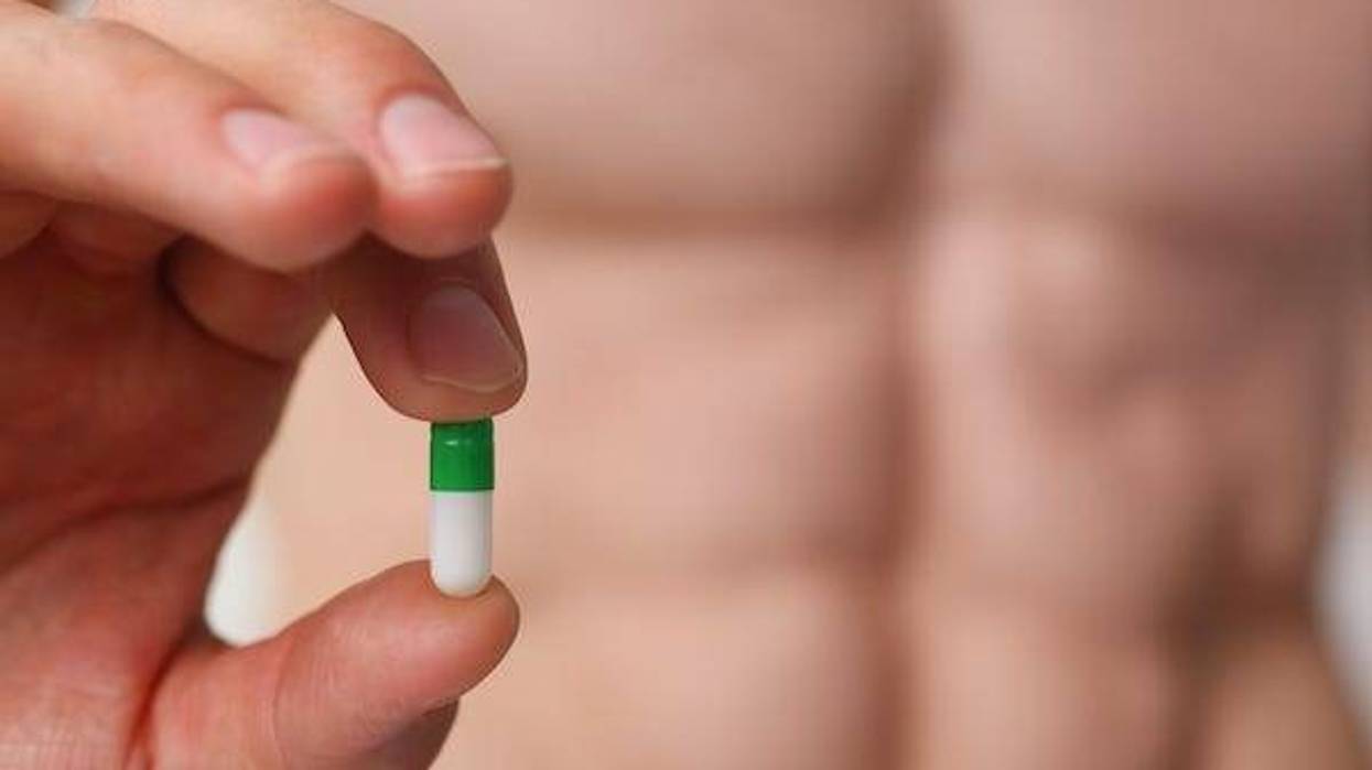 Muscular man holding pill in front of camera