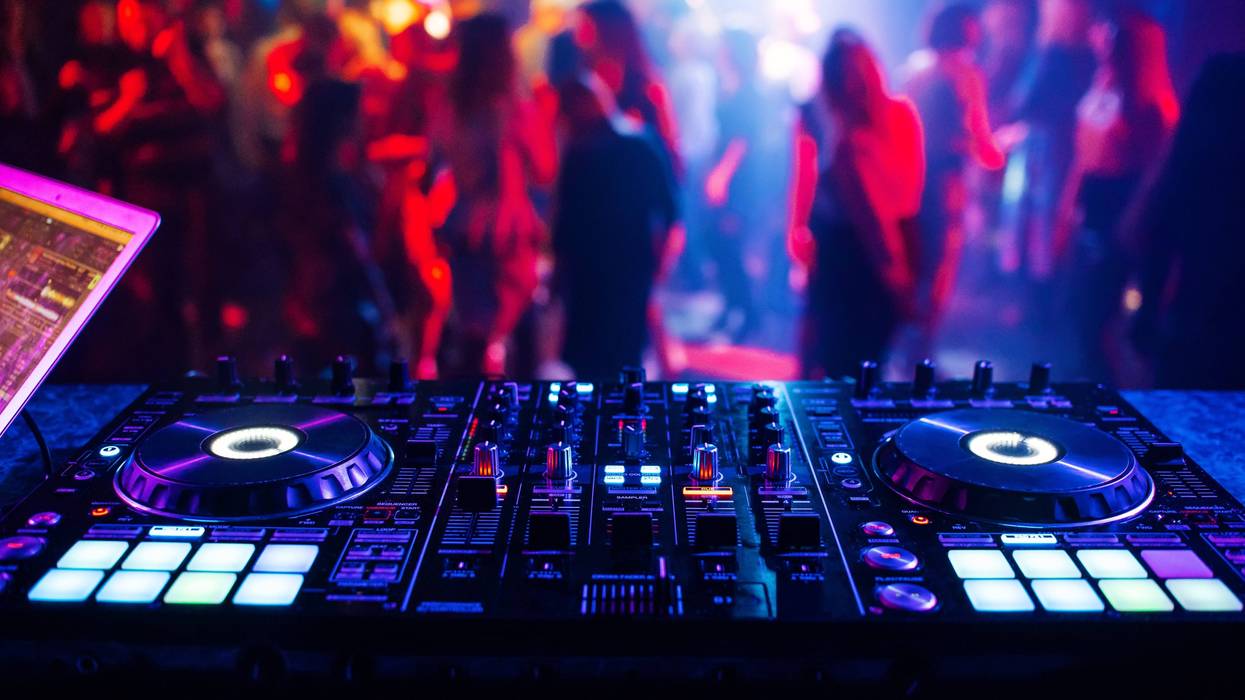music controller DJ mixer in a nightclub at a party against the background of blurred silhouettes of dancing people