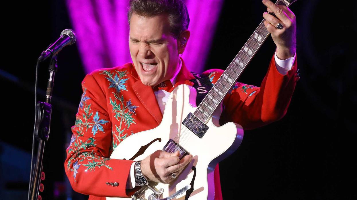 Musician and singer Chris Isaak performs in a red suit with a white guitar