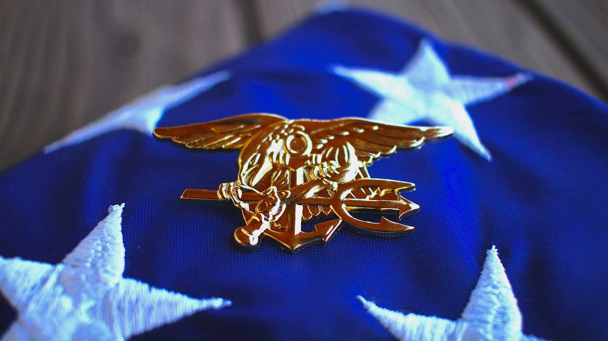 Navy SEAL trident rests atop a folded American flag.