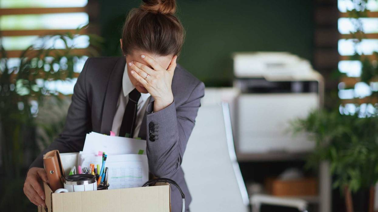 New job. unhappy modern female employee in modern green office in grey business suit with personal belongings in cardboard box.
