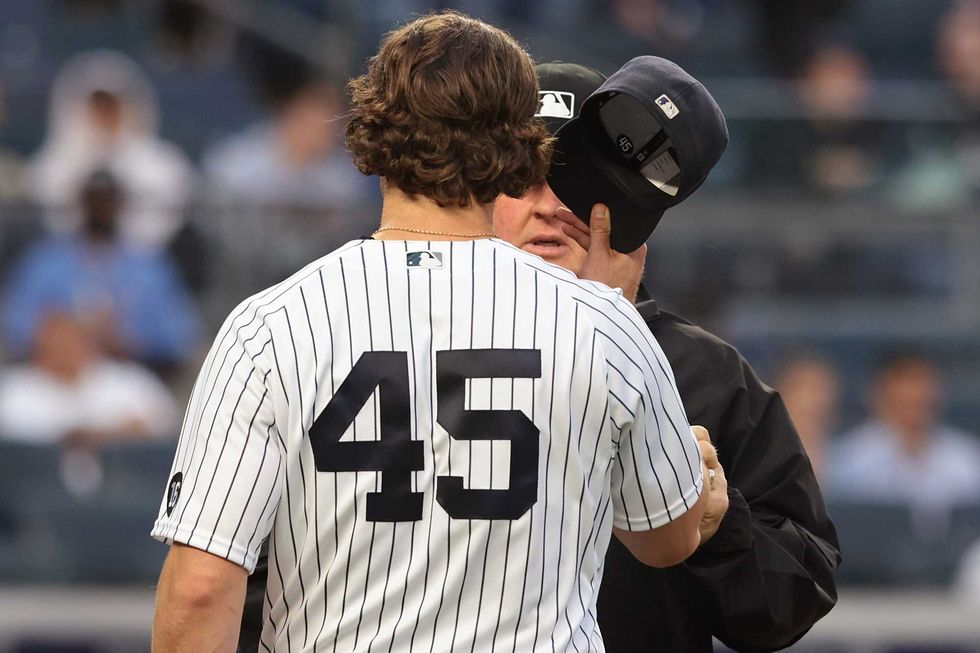 New York Yankees starting pitcher Gerrit Cole (45) hands his cap to umpire Bill Miller (26) for examination after the third inning against the Kansas City Royals at Yankee Stadium.