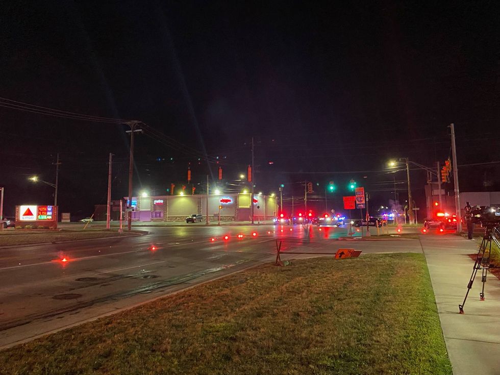 Night scene at a street intersection with police lights, road flares, and a news camera.