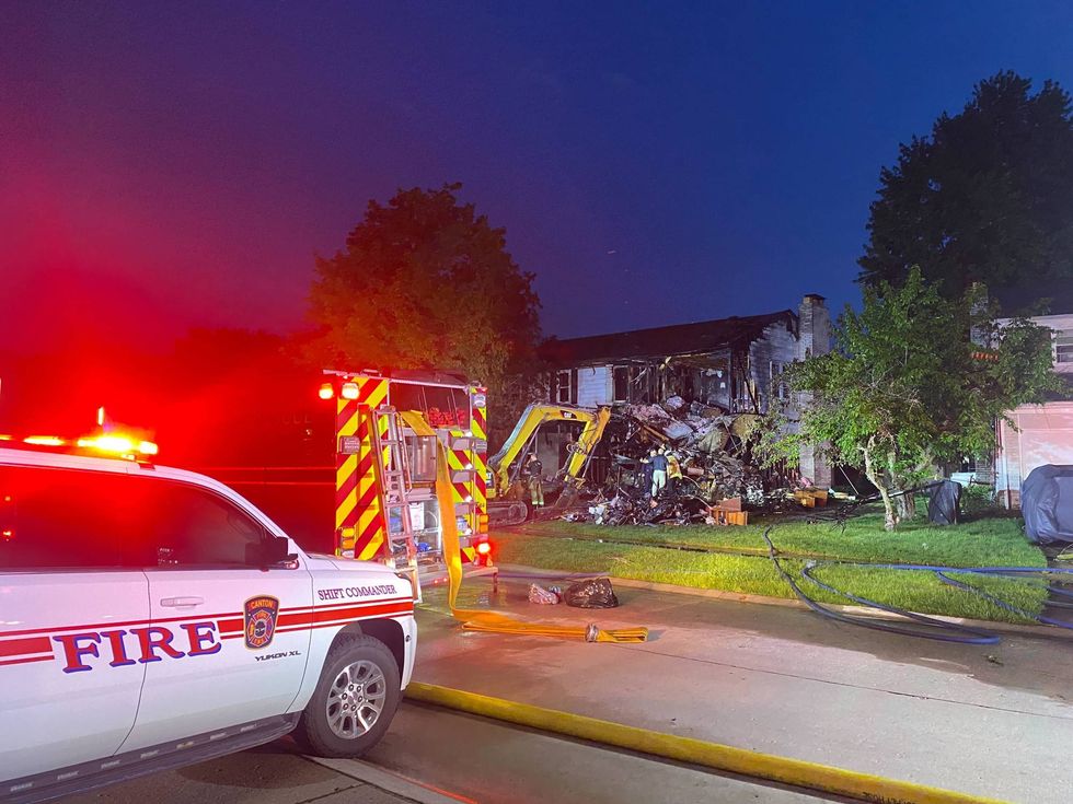 Night scene: Fire department vehicles and excavator at a house severely damaged by fire.