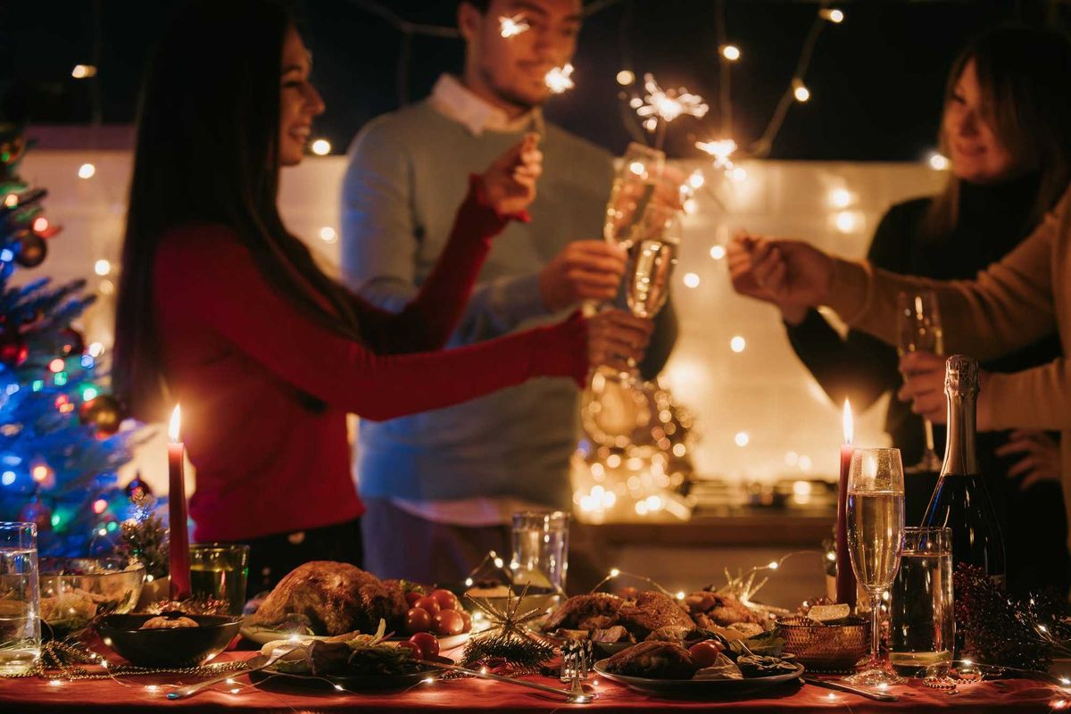 Night shot of people toasting with champagne and holding sparklers while having New Year party at home