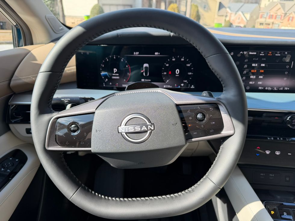 Nissan car interior: black steering wheel with logo, modern digital instrument cluster & infotainment screens.