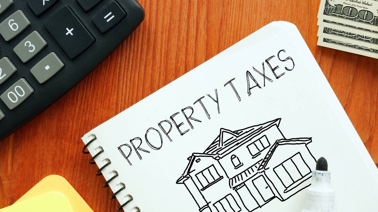 Notebook with 'PROPERTY TAXES' and house drawing, calculator, and $100 bills.