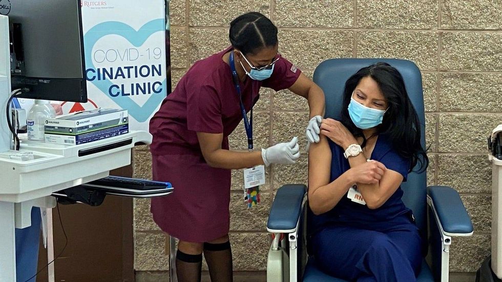 Nurse Maritza Beniquez, center, receives the first COVID vaccine shot in New Jersey at University Hospital in Newark as state Health Commissioner Judy Persichilli, right, looks on, Dec.15, 2020.