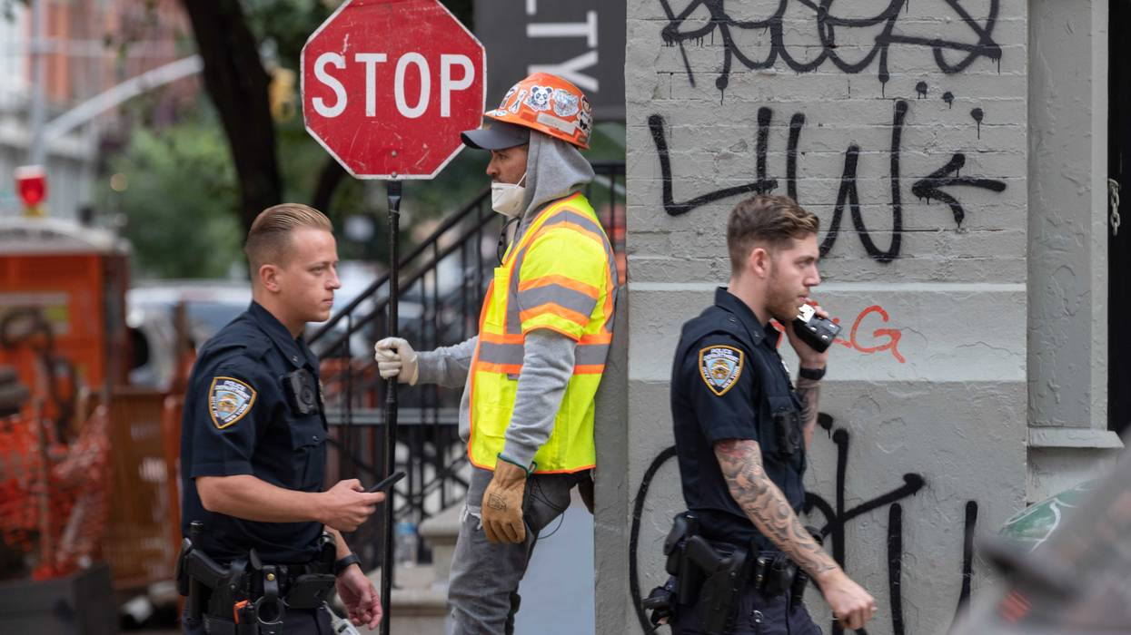 NYPD officers without masks walk past a construction worker holding a stop sign as the city continues Phase 4 of re-opening following restrictions imposed to slow the spread of coronavirus on September 16, 2020 in New York City.