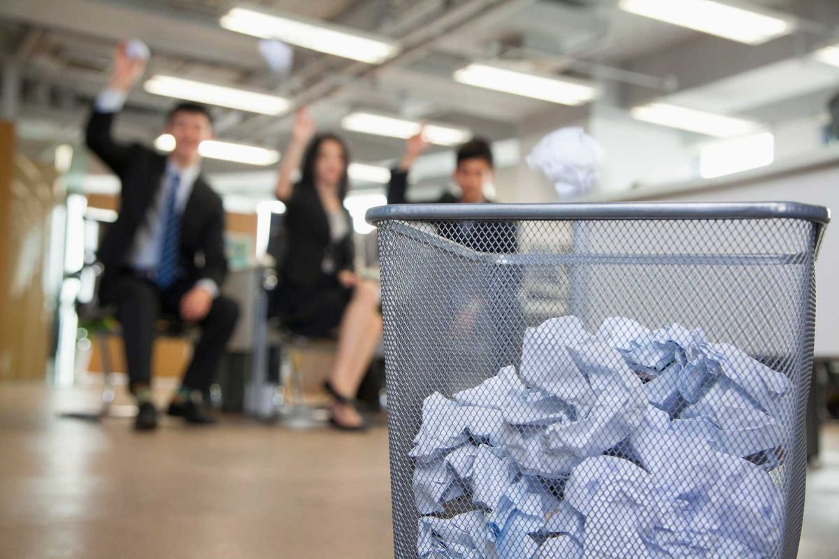 Office workers throwin paper into a trash can.