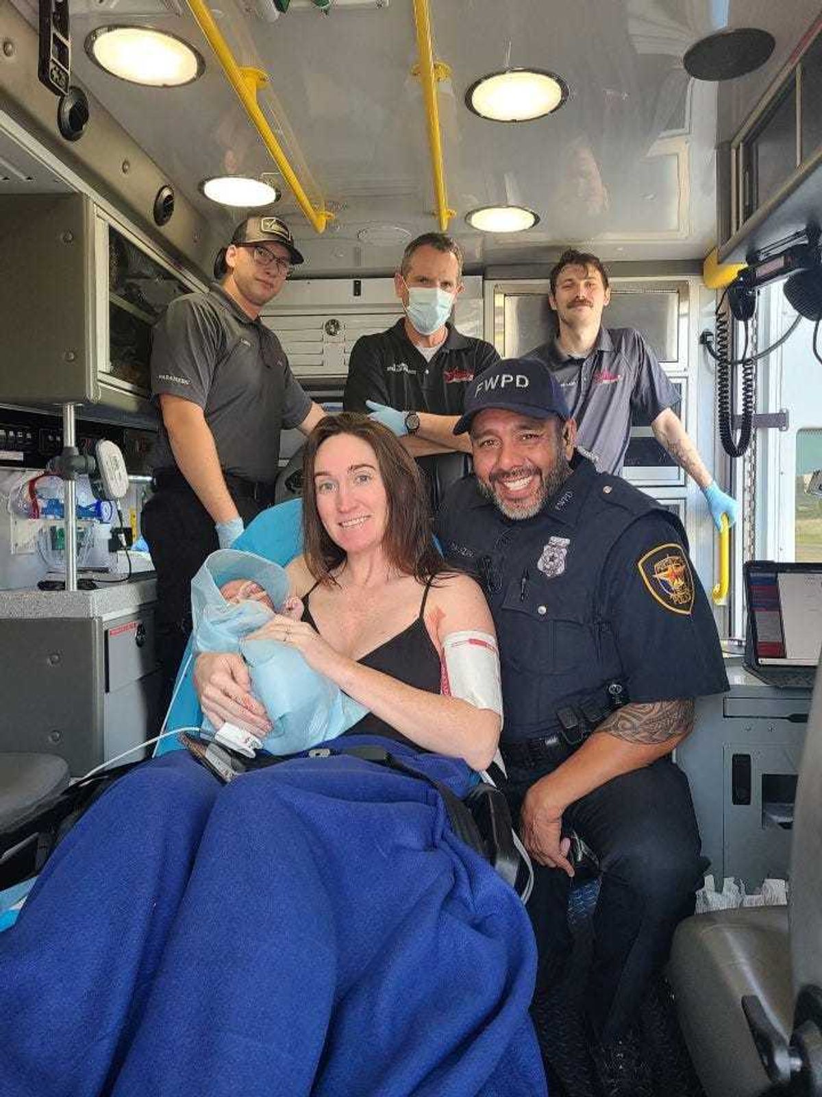 Officer Salazar and the woman he helped deliver her baby pose for a photo inside of an ambulance.