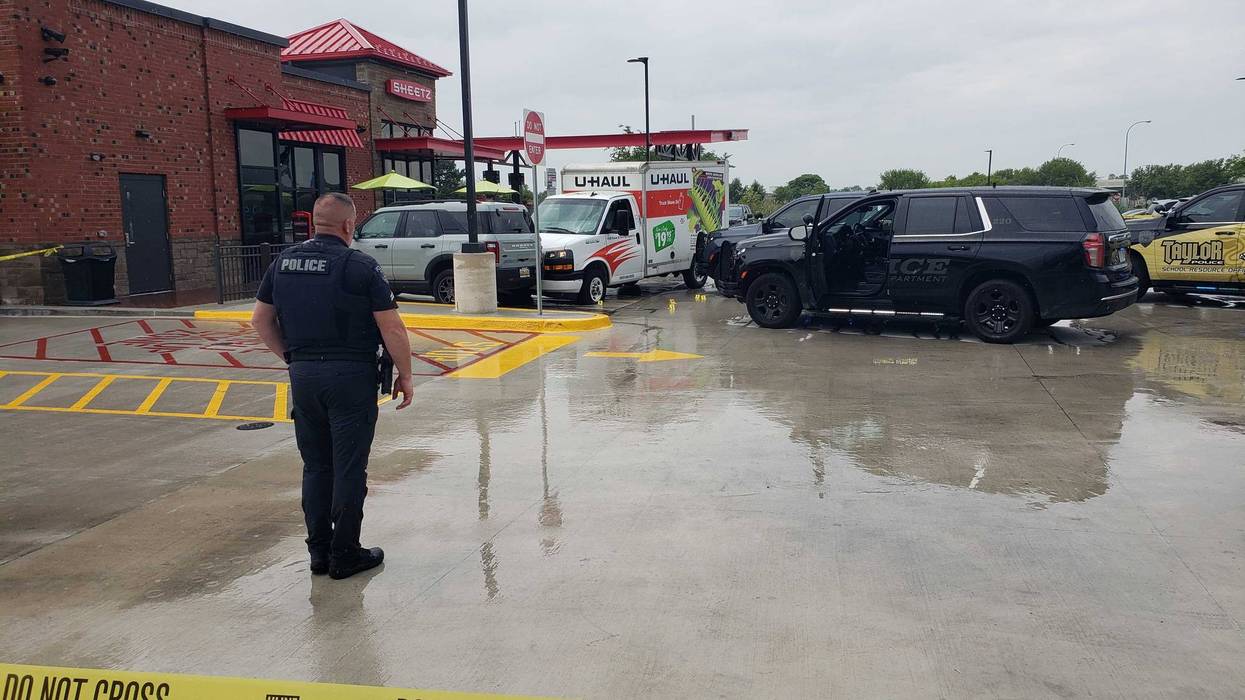 Officer stands by "Police Line Do Not Cross" tape at a Sheetz store with multiple police vehicles.