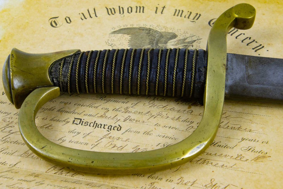 Old Saber lying on a historic document of Union Army discharge Certificate from 1863 with focus on Handle