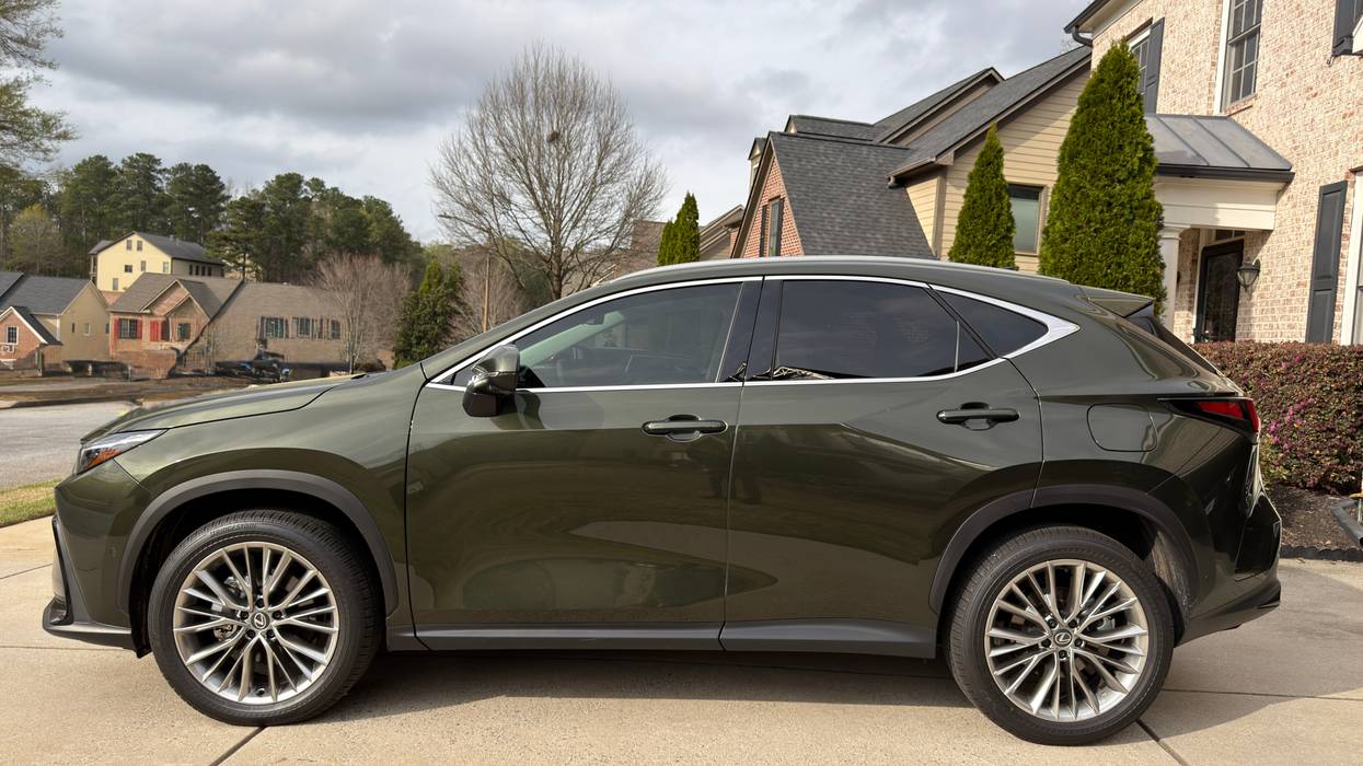 Olive green Lexus NX SUV parked on a driveway with houses and trees in the background.