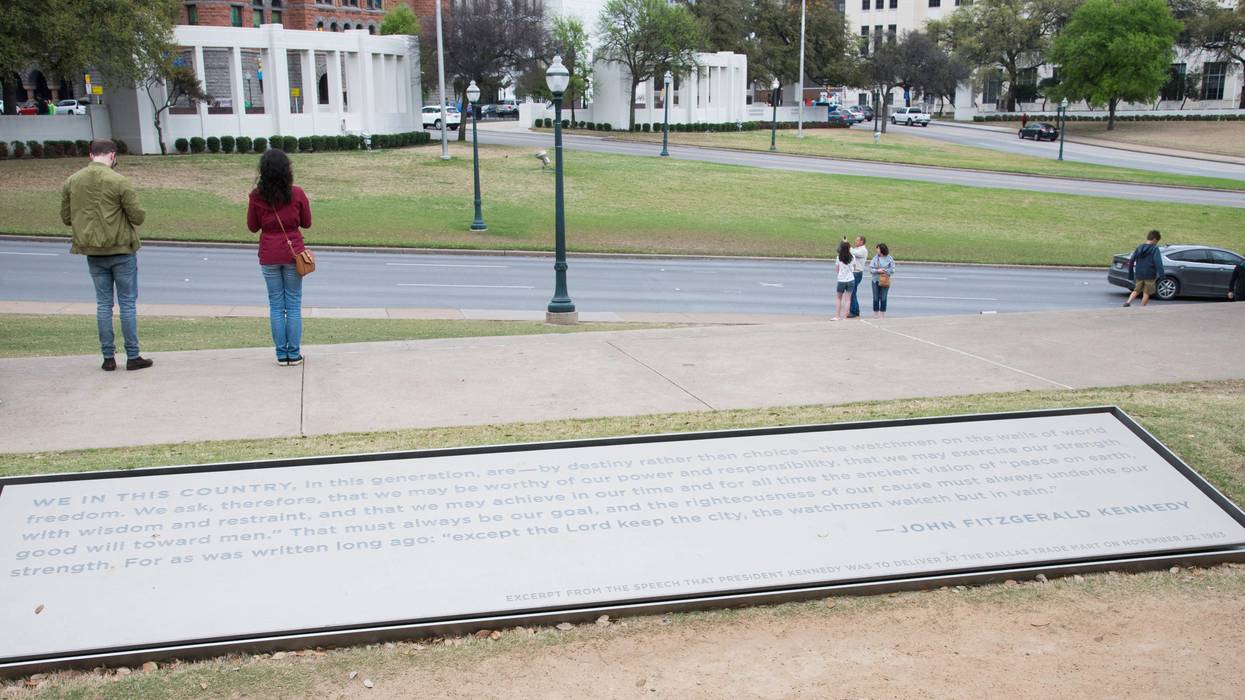 On March 17, 2017, two people pay their respects to John F. Kennedy on the sidewalk above Elm Street in Dealey Plaza, Dallas, Texas.